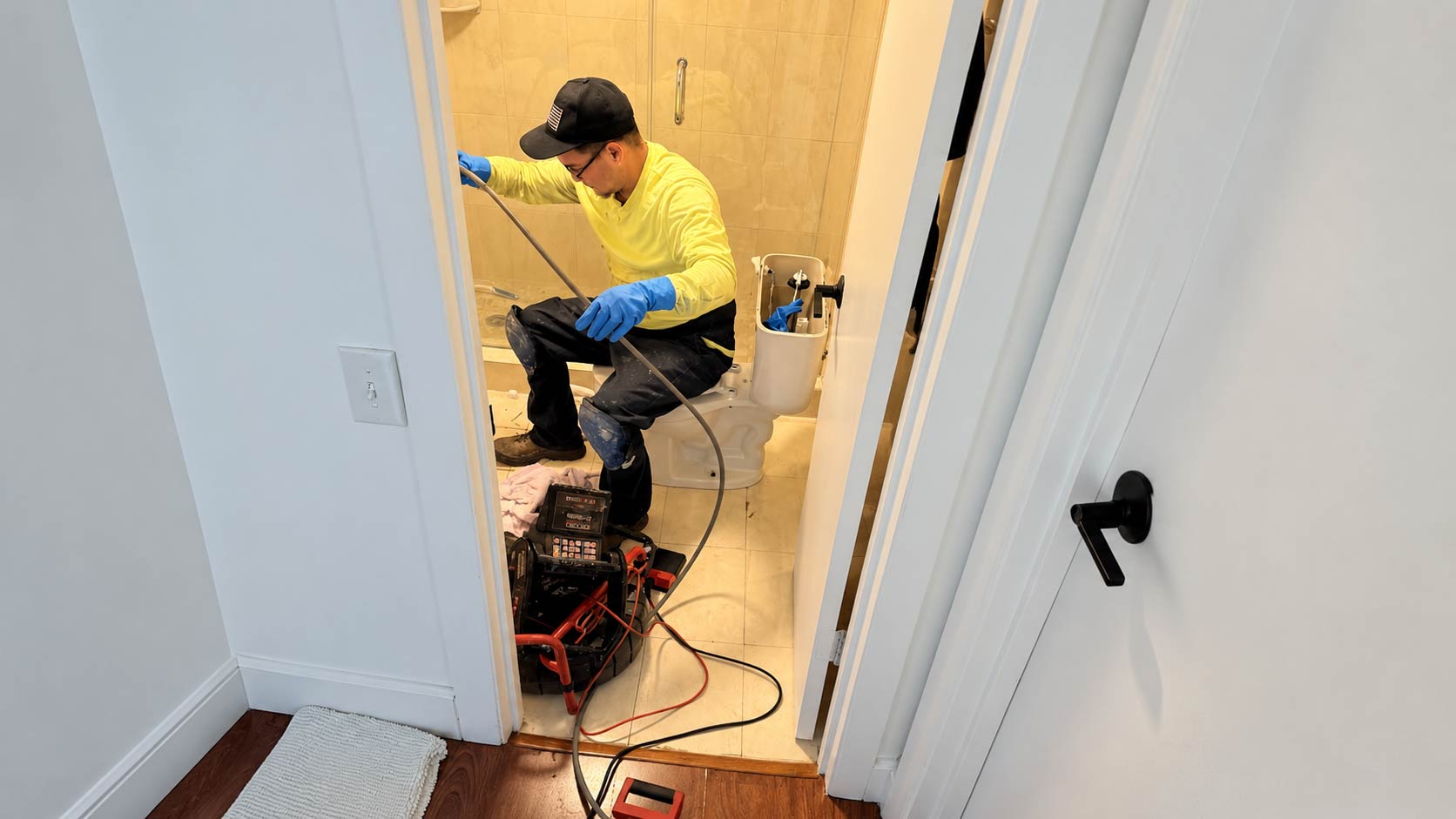 Plumber using drain equipment while inspecting a bathroom toilet